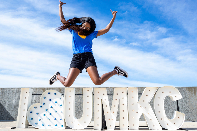 student jumping in front of I heart UMKC sign