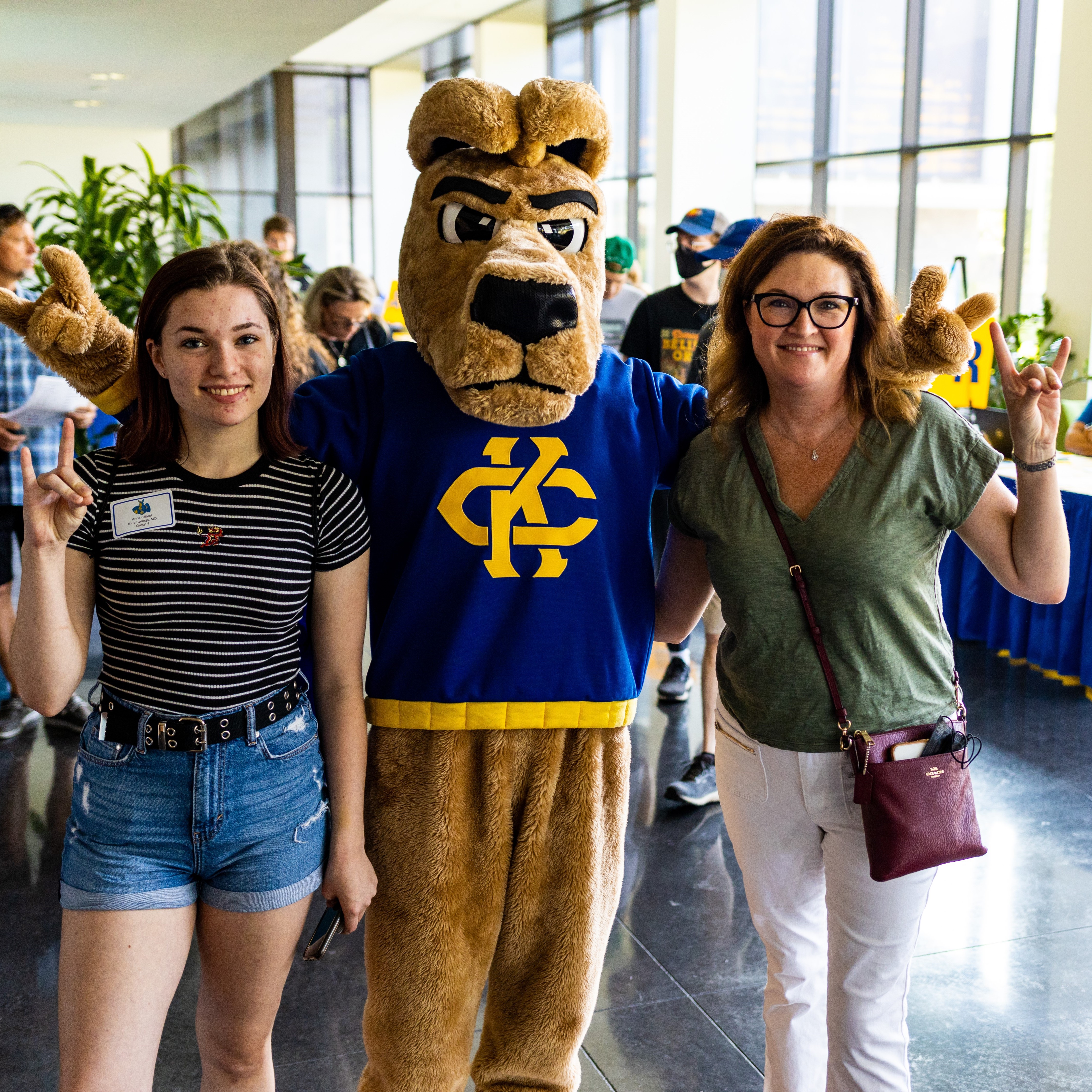 an incoming student and her mother make the Roo Up hand sign while posing with the KC Roo mascot