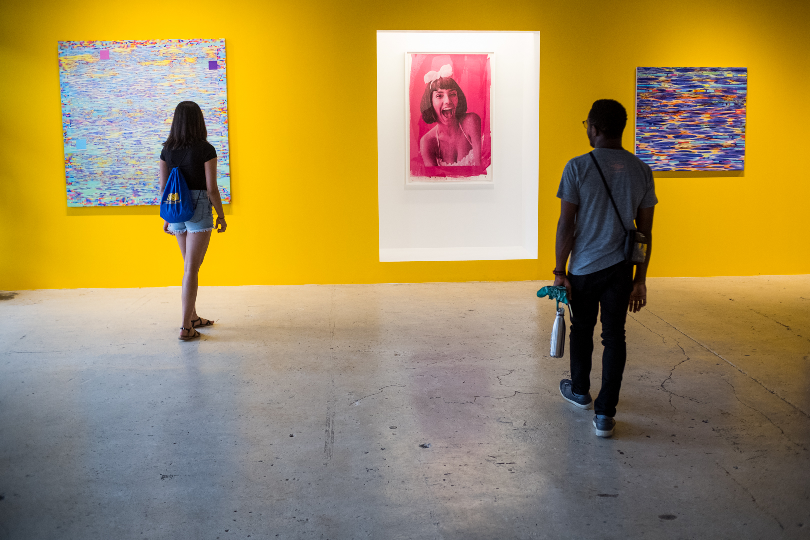 two students, their backs to the camera, view art in a gallery during first fridays in the crossroads