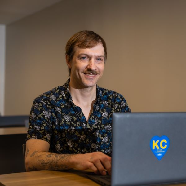 Hourly Amazon employee Cody Truitt sits at a desk with an open laptop in front of him. Cody looks pleases because he graduated from UMKC with a bachelor's degree.