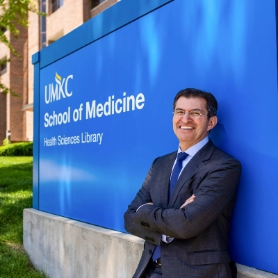 Dean Alexander Norbash leaning against the sign outside of the School of Medicine.