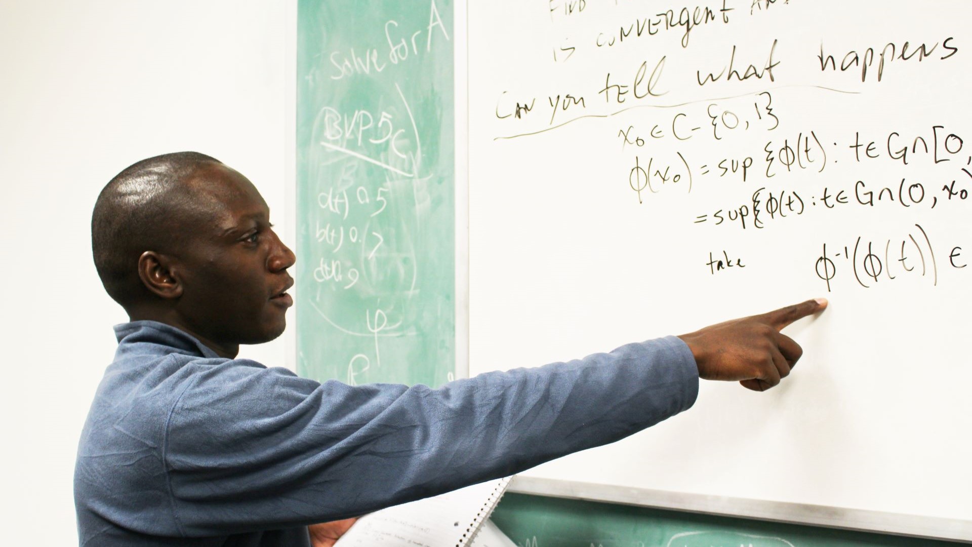 photo of student pointing to a math equation in a classroom