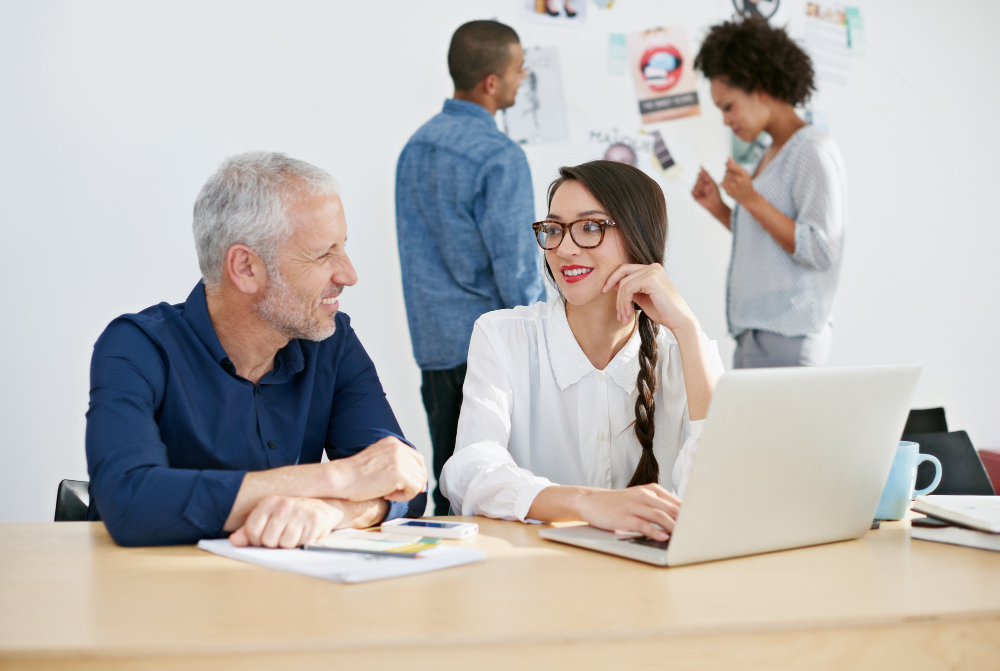 two individuals working together at a laptop with two others in the background