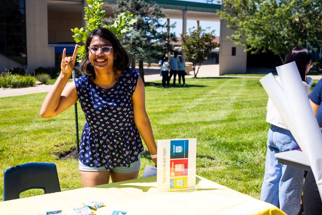 a student looks happy while giving the Roo Up hand sign while at a table at the ISAO resource fair