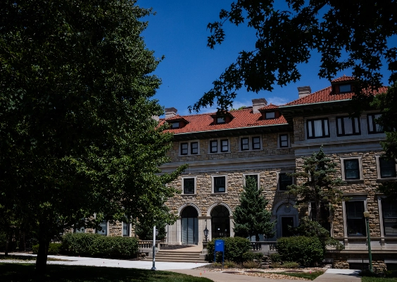 The front of a stone building with a red tile roof on campus during a sunny day. 