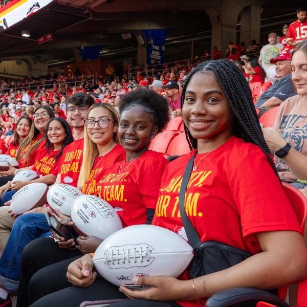 UMKC students dressed in Chiefs red t-shits sit in seats at the stadium after being celebrated on the field.