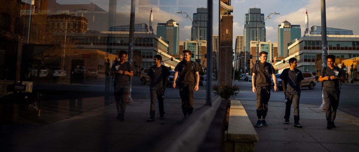 Three dental students wearing scrubs walk by a glass building in the Crossroads Arts District. They are smiling and enjoying a sunny day.