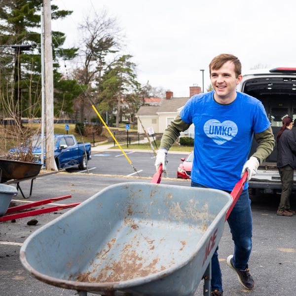 Student looks happy pushing an empty wheelbarrow while volunteering to create a community garden. 