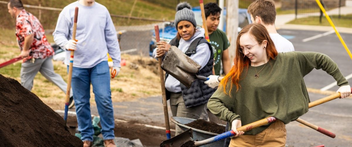 Two students shovel dirt into wheelbarrows to fill garden beds on campus