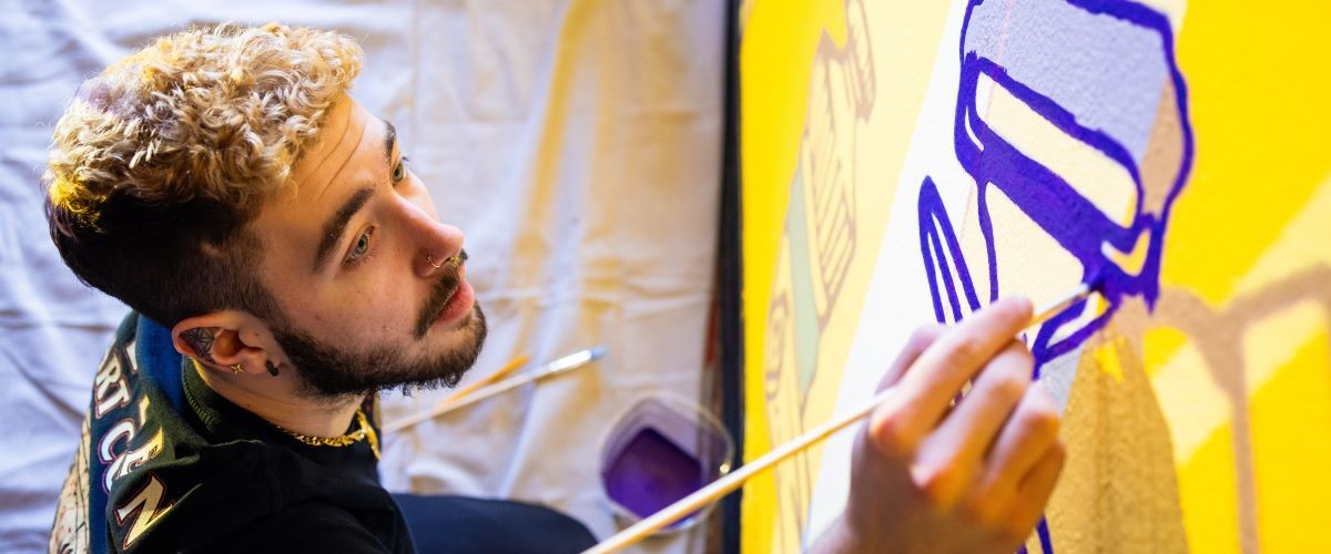 An art student paints a mural on a wall