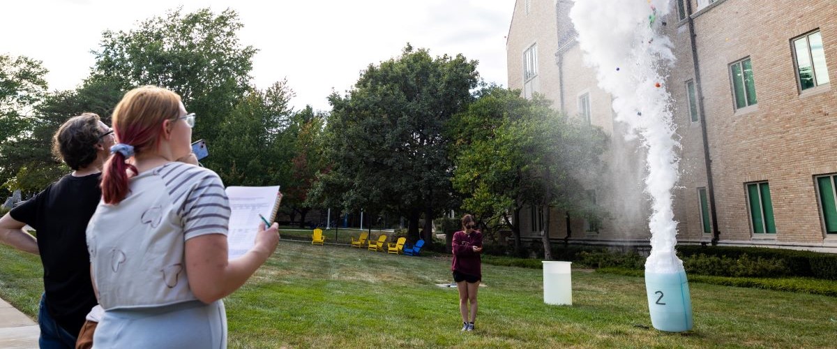 Two students watch an explosion in a trash can during a science class outside