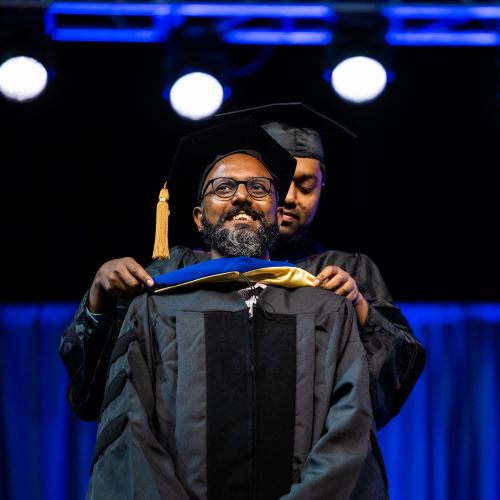 UMKC graduate student receives graduation hood from faculty member advisor during the May hooding ceremony