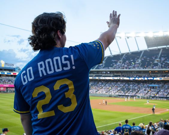 UMKC student shown from the back wearing a Go Roos jersey and waving to the other side of Kauffman Stadium where the Royals play