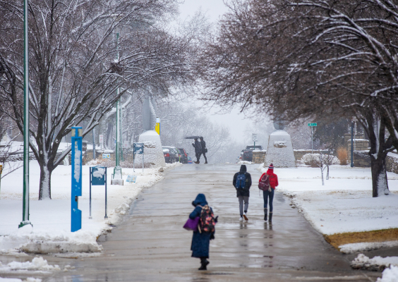 View of students walking on a main campus walkway during a winter snow storm.