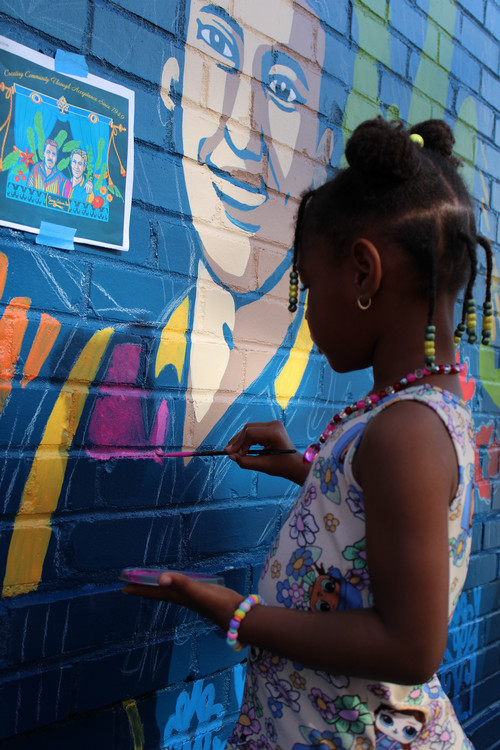 Girl is painting a mural traced on a brick wall.