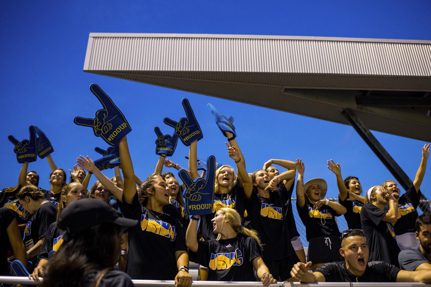 students with foam fingers cheering in the stands at a UMKC soccer game