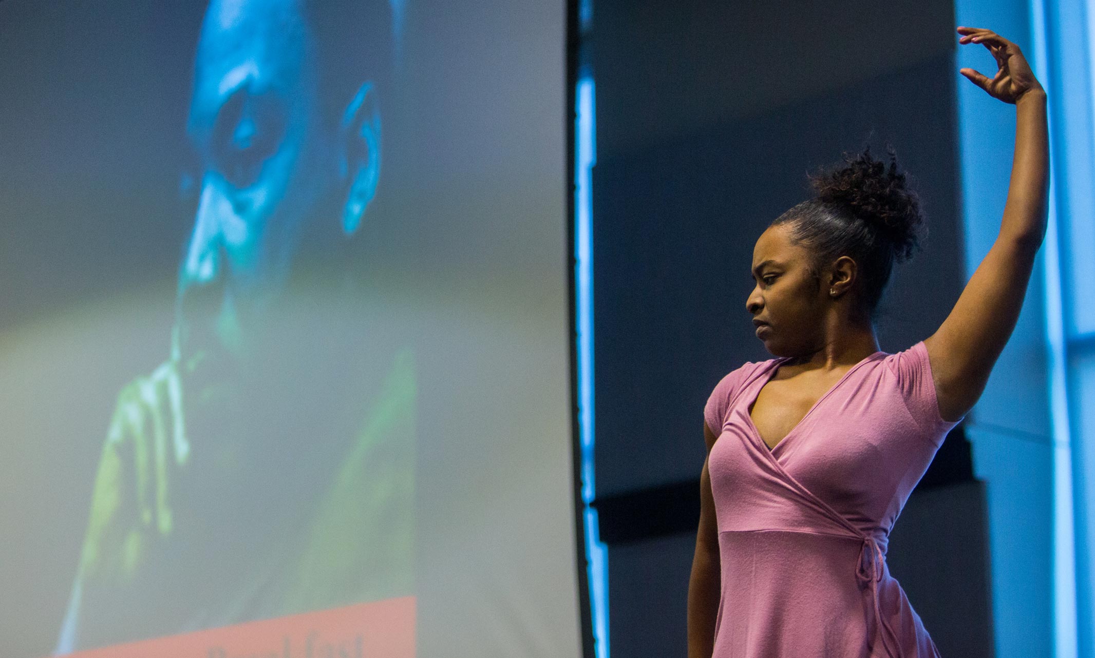 Black female student performs a dance on stage with a photo of Martin Luther King Jr. in the background during the TAASU Freedom Breakfast