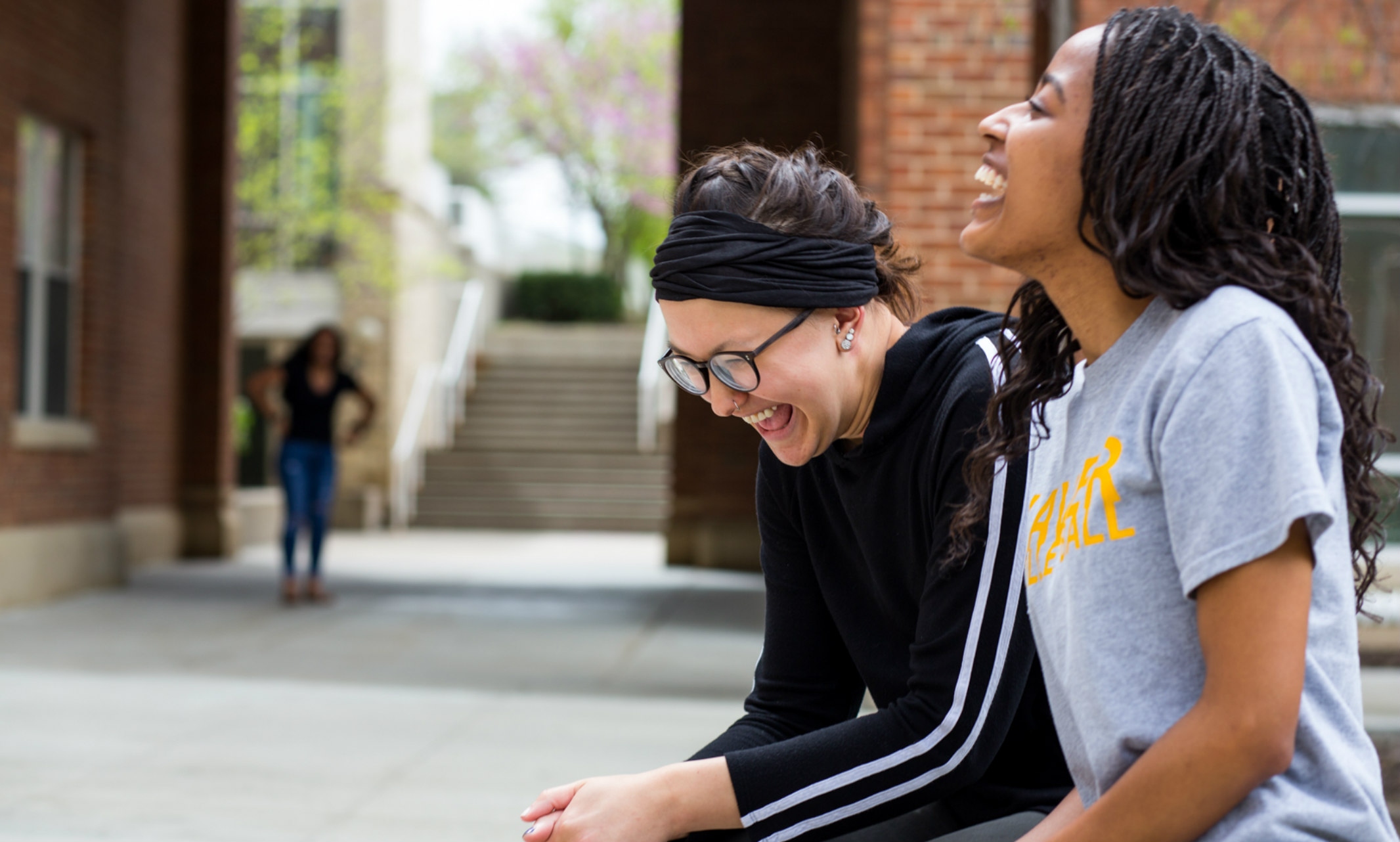Two female students laughing outside a UMKC residence hall.