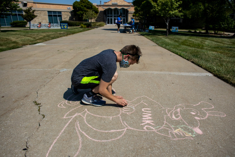 a student draws a chalk roo on the sidewalk