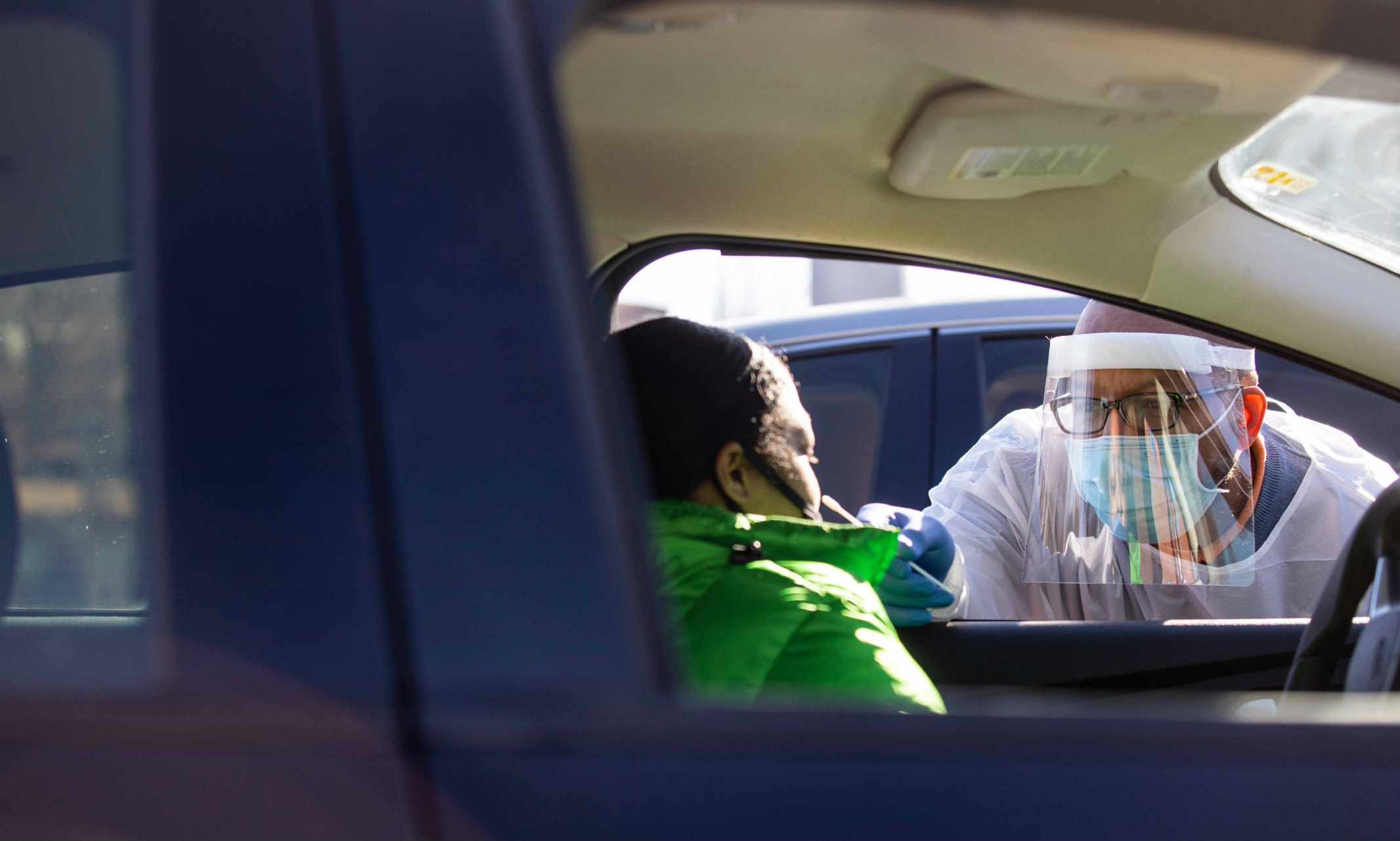 An image of Obie Austin wearing a face mask talking to a person sitting in a car.