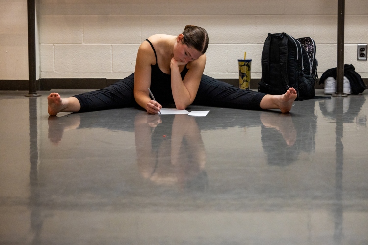 A dancer sits on the floor doing the splits writing with her chin resting in her hand