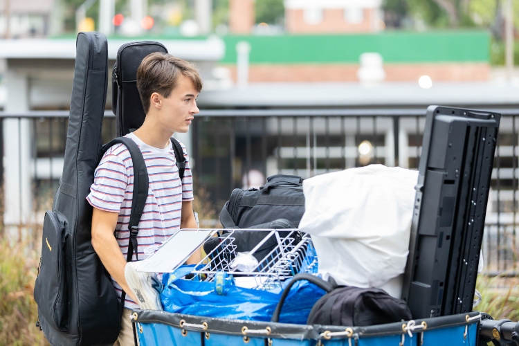 A student pushes a bin during move in at Oak Street Residence Hall