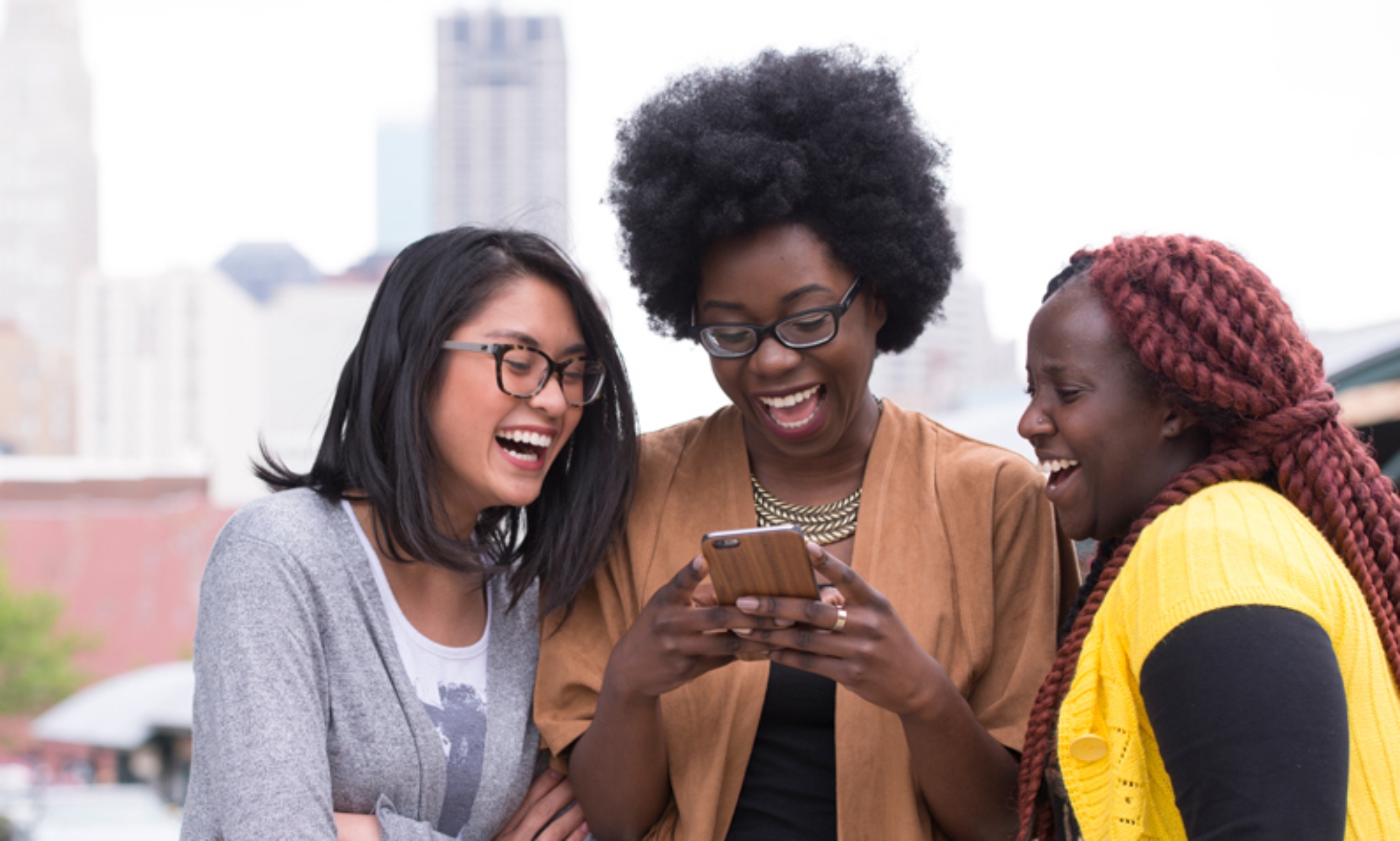 three women look at a cell phone and laugh