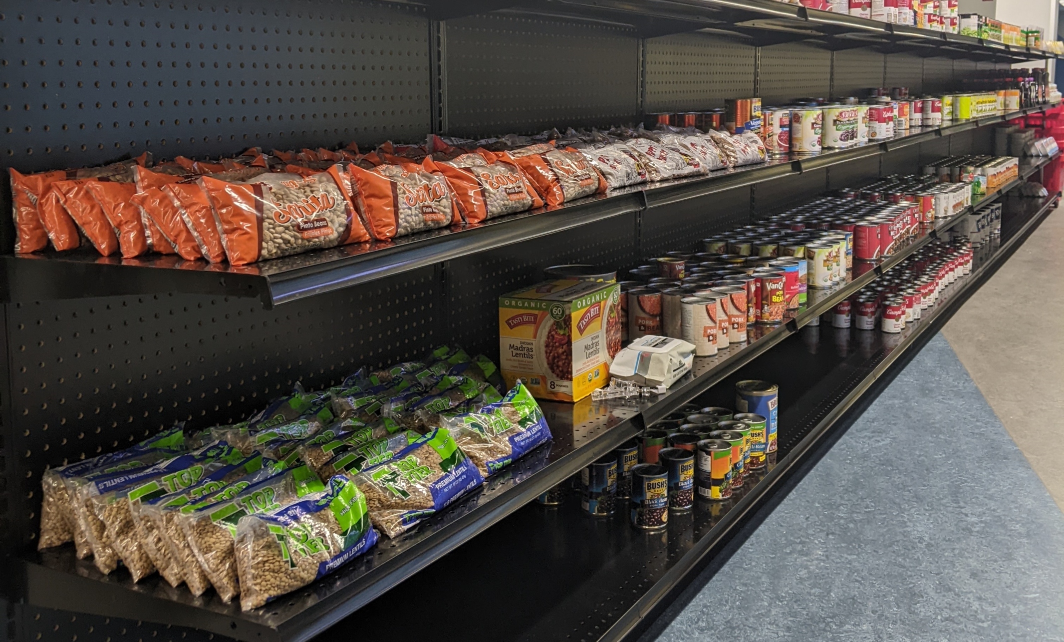 Students and faculty file into a grocery aisle of the Agrawal Care Center. The aisle features boxed and canned food items.  