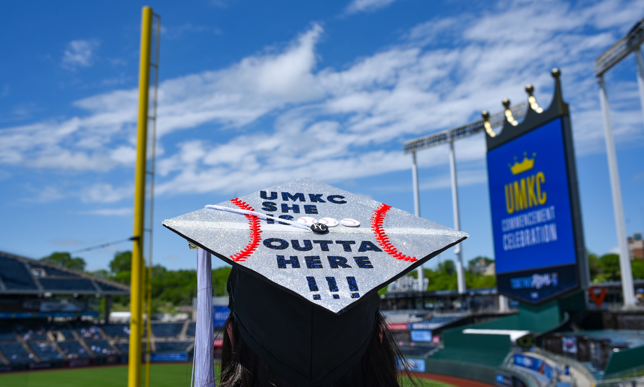 Graduate cap that says "UMKC, she's outta here" with the Royals Crown Vision screen in the background