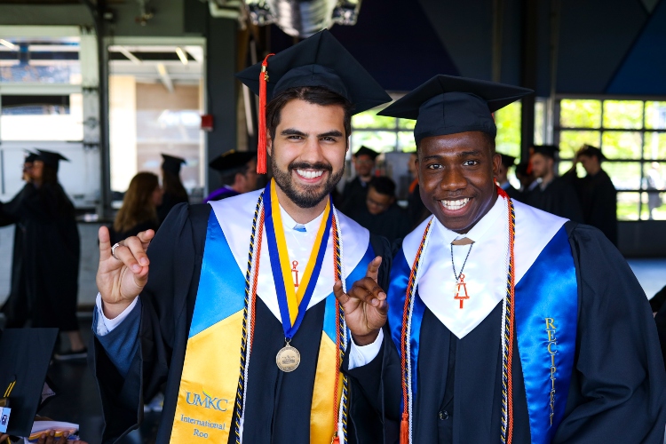 Two graduates doing the Roo Up hand gesture