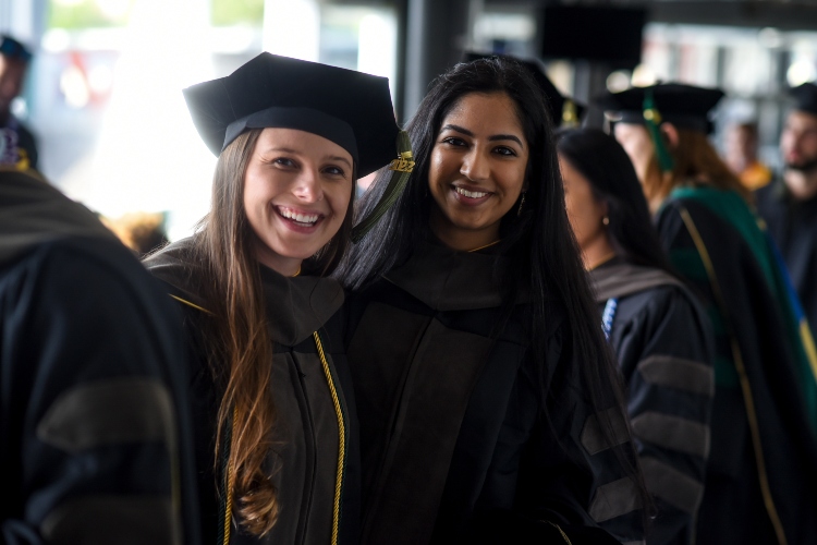 Two women in graduation robes smile