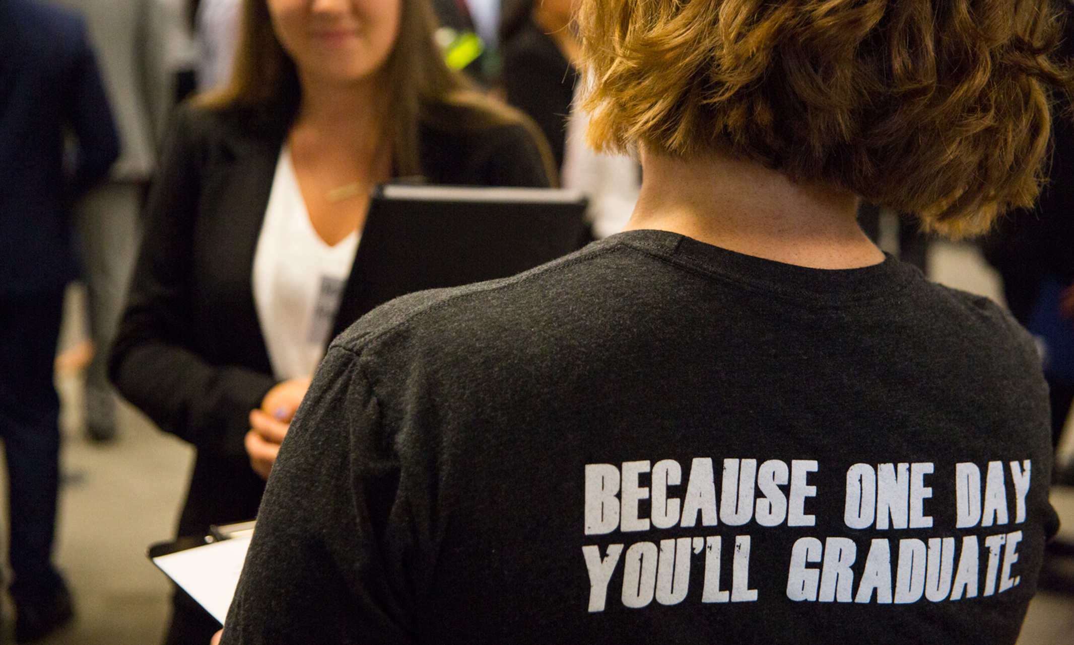 Person faces away, the back of their shirt reads, "Because one day, you'll graduate."