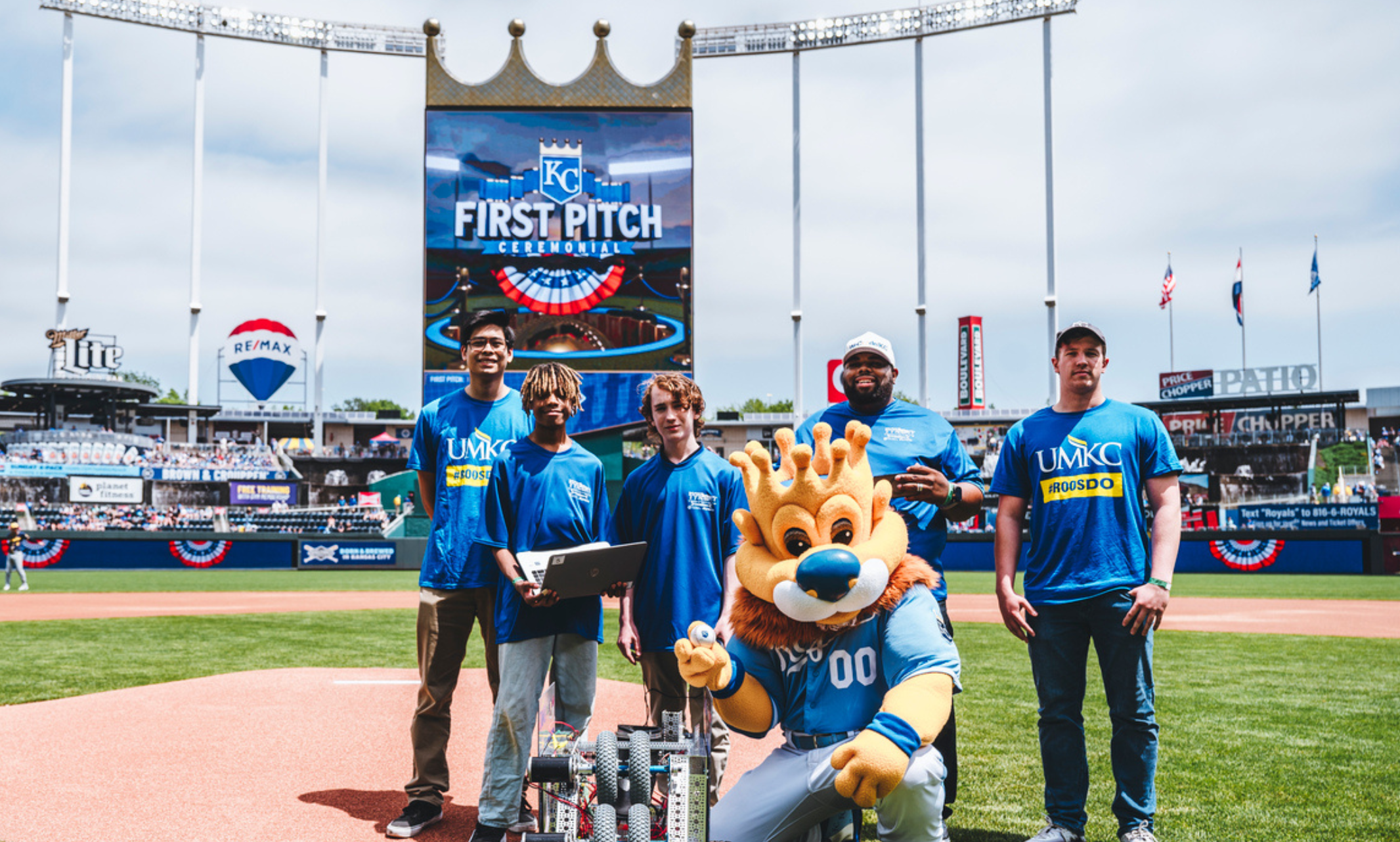 UMKC and local high school students stand on the pitcher's mound with Sluggerrr in Kauffman Stadium