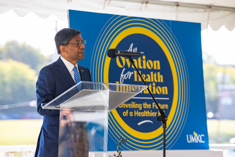 Mauli Agrawal stands at a podium. Behind him is a blue banner that says "An ovation to health innovation"
