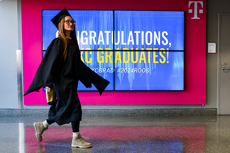 Female in grad cap walking in front of UMKC Commencement sign