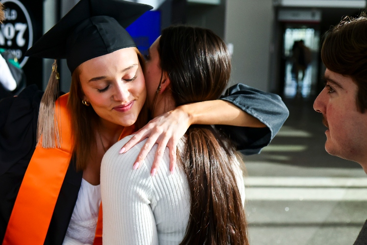 A female graduate hugging another person.