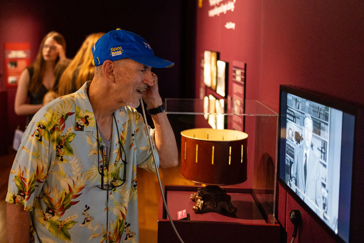 Man in a UMKC Hat using audio device to listen to Walt Disney speak on video