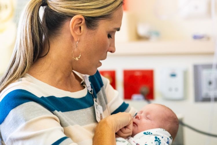 Amy Robertson holds a small baby and gently touches its face while singing a lullaby to it