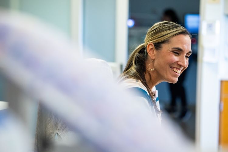 Amy Robertson smiles to a baby and mother while sitting in a NICU hospital room