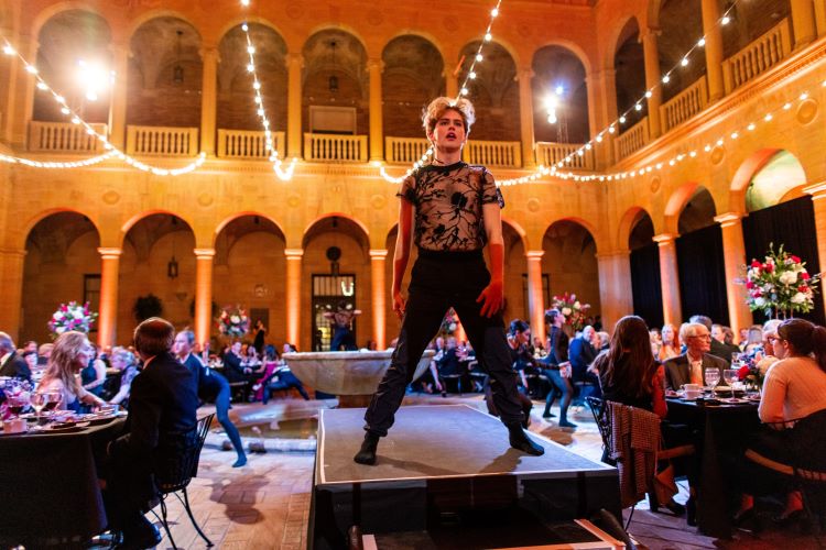 A dancer stands on a platform in Rozzelle Court, audience members look on