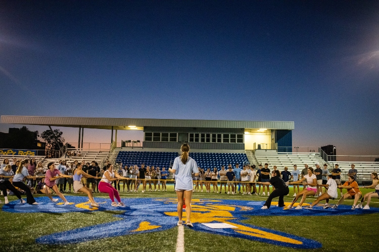 two groups of Greek Life students play tug of war at Durwood with the sunsetitng in the background as a judge and audience watch on