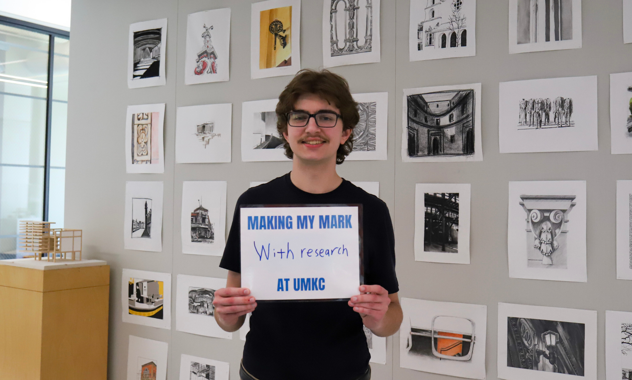 Aaron Beckman holds a sign that says "Making my mark with research at UMKC"