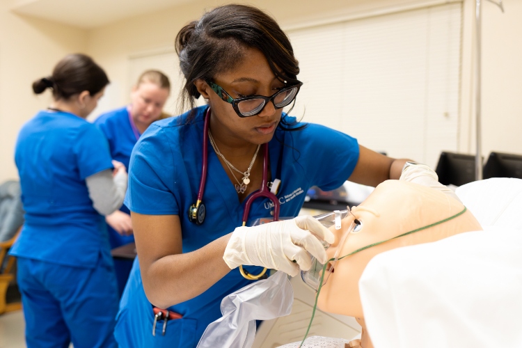 A nursing student in blue scrubs puts an oxygen mask on a mannequin