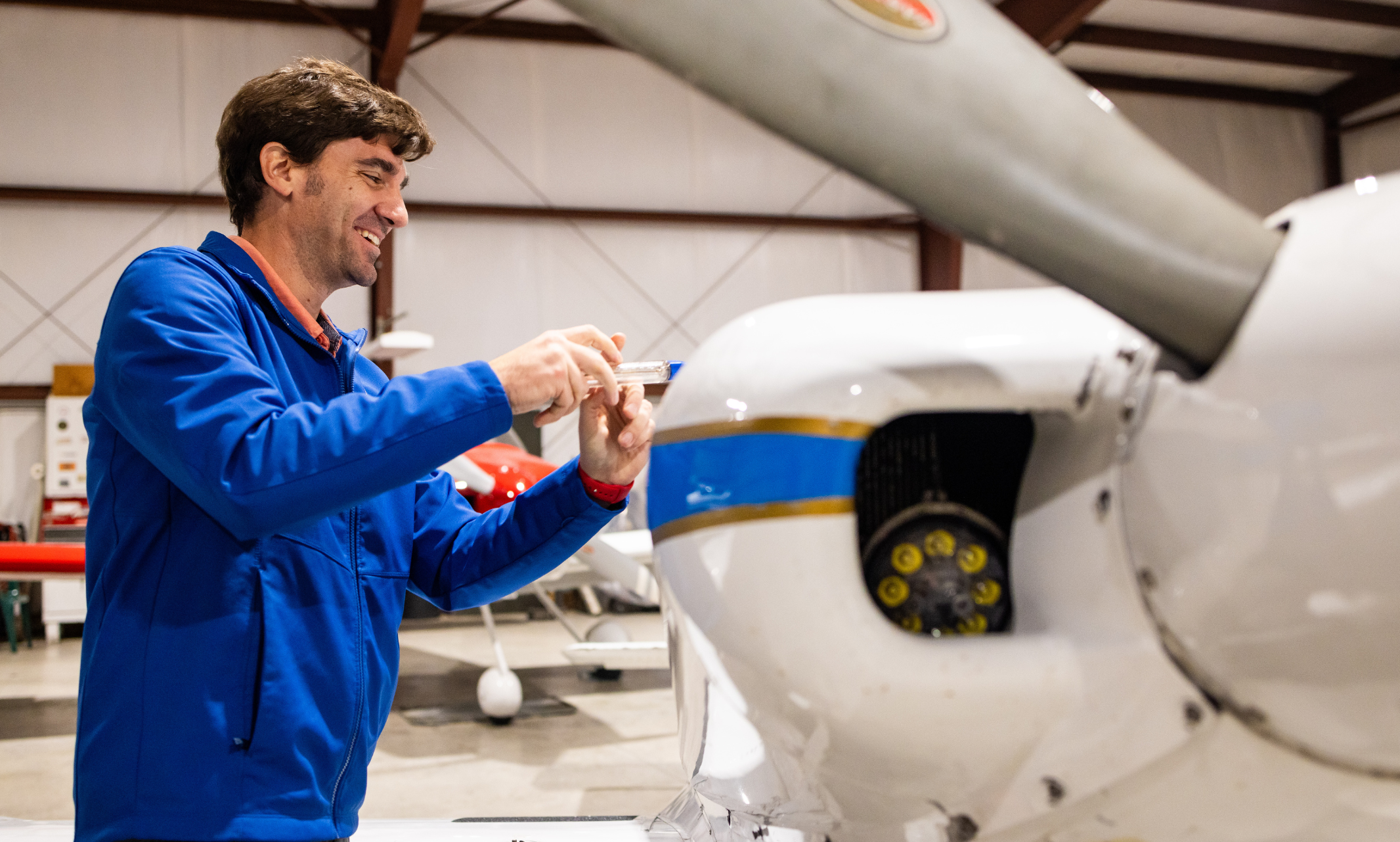 Travis Fields uses a screwdriver and is seen smiling as he works on his plane.