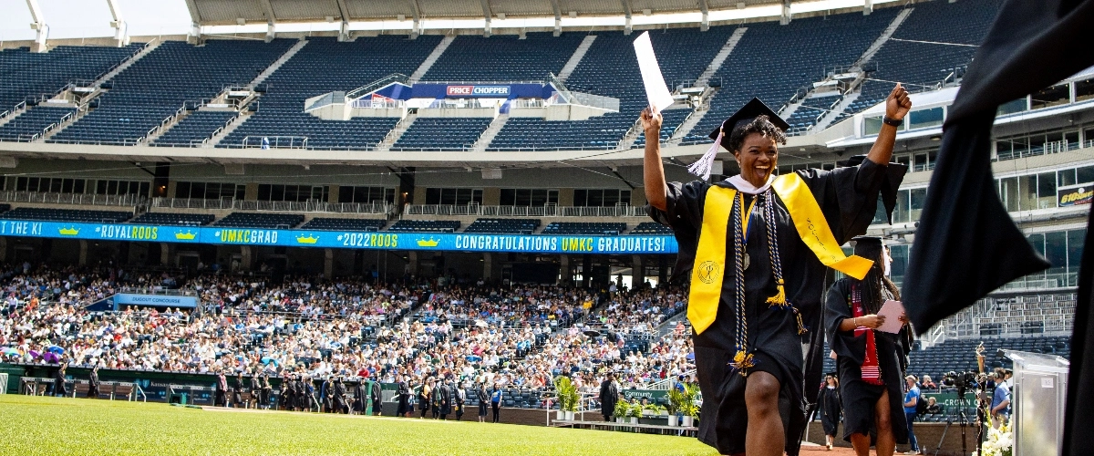 UMKC graduate holds hands up in celebration at Commencement ceremony at Kauffman Stadium