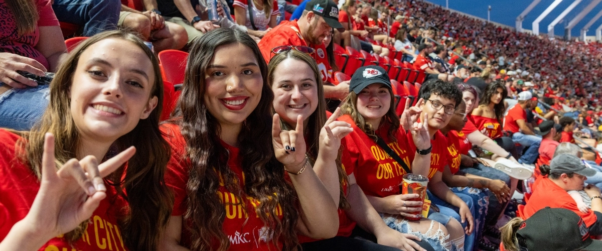 UMKC students taking a selfie while sitting in stands at Arrowhead Stadium during a Chiefs preseason game.